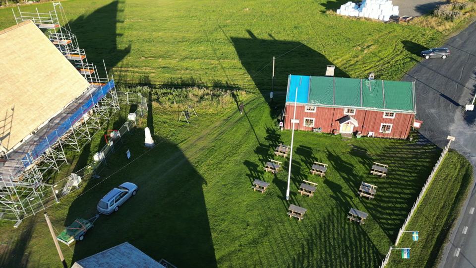 Drönarbild över ett rött hus med ställning runt taket, åkrar och sjö i bakgrunden