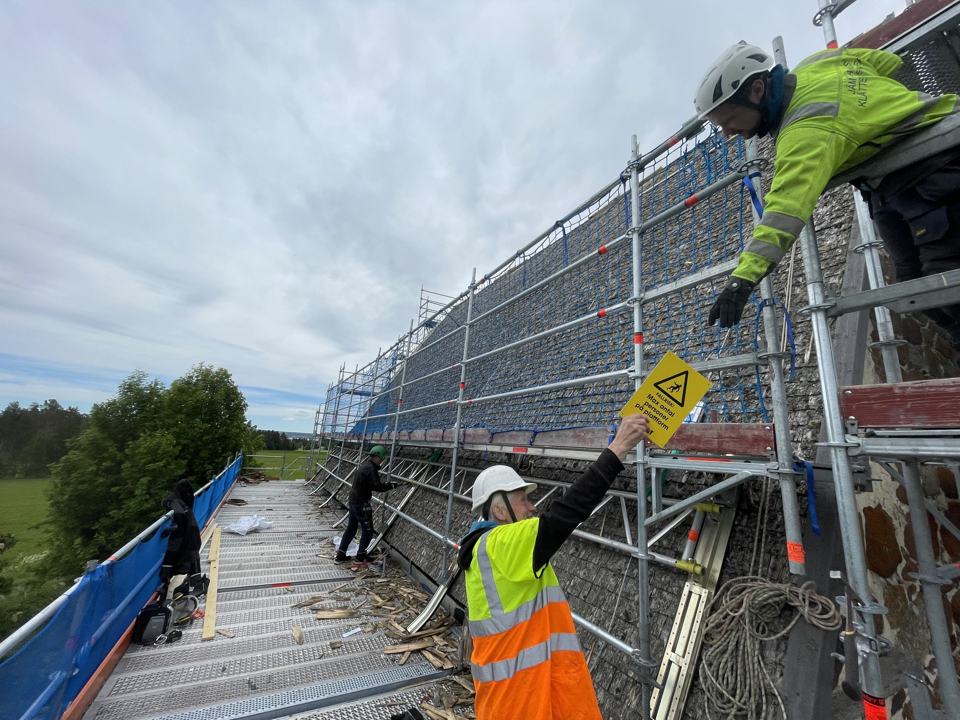 Montörer i hjälm och varselkläder arbetar på ställningens plan