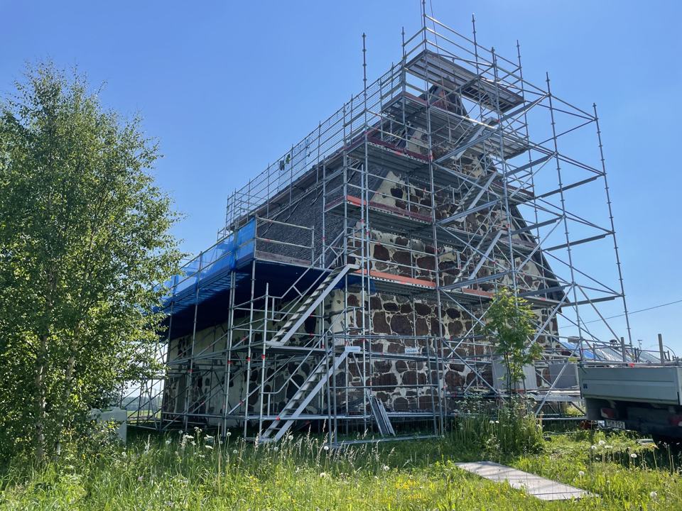Hög fasadställning med trapptorn runt en stenbyggnad en sommardag