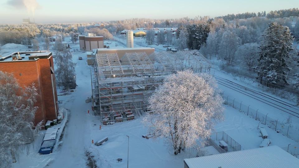 Drönarbild en vinterdag: stort bygge helt inbyggt i ställning, rimfrost på träden och snö runt omkring